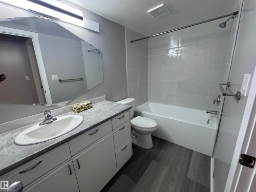 Bathroom featuring a white vanity with an integrated sink, patterned countertop, and a modern geometric mirror - 6441 180 Street, Edmonton, AB 