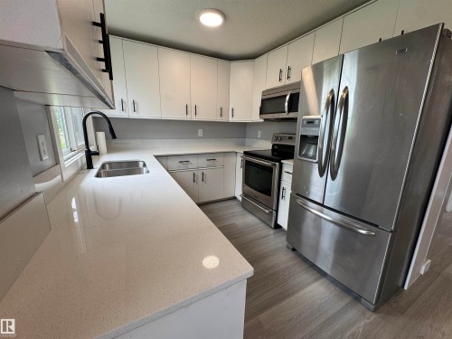 Kitchen featuring white cabinetry with matte black hardware, light-toned countertops, stainless steel appliances, and wood-finish flooring - 6441 180 Street, Edmonton, AB 