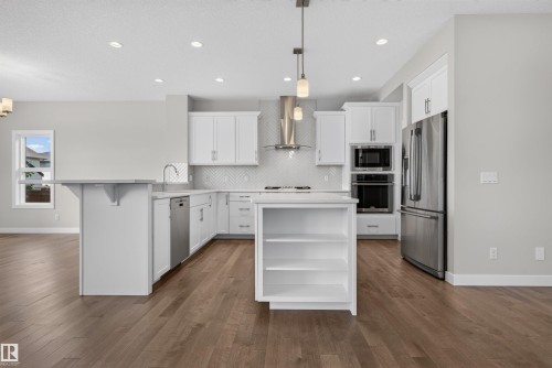 Contemporary kitchen featuring white cabinetry, stainless steel appliances, wood-finish flooring, a central island with open shelving, and pendant lighting - 9432 229 Street, Edmonton, AB 