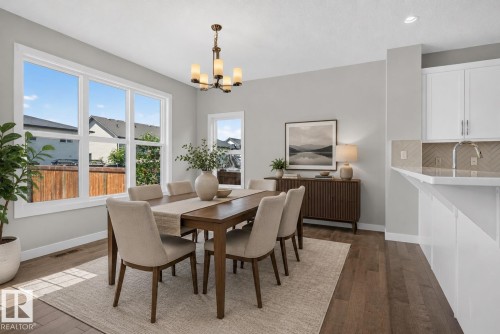 Dining area featuring wood-finish flooring, a contemporary chandelier, and a wall of windows - 9432 229 Street, Edmonton, AB 