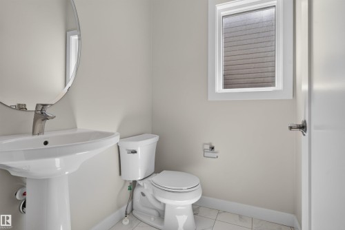 Pedestal sink with chrome faucet, oval mirror, white toilet, and window with privacy blinds - 9432 229 Street, Edmonton, AB 