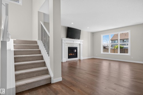 Living area featuring wood-finish flooring, a fireplace with a decorative mantel and mosaic tile surround, and large windows - 9432 229 Street, Edmonton, AB 