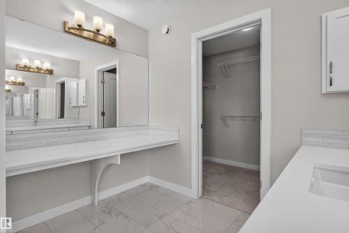 Vanity area featuring a quartz countertop with an integrated sink, full-width mirror, and a three-light fixture - 9432 229 Street, Edmonton, AB 