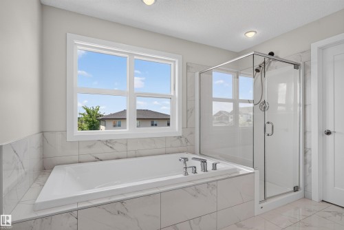 Soaking tub with surrounding white marble-look tile, large window, and glass-enclosed shower with chrome fixtures - 9432 229 Street, Edmonton, AB 