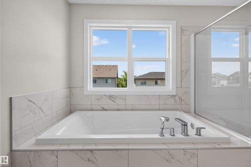 Built-in soaking tub with polished chrome fixtures, surrounded by large format marble-look tile - 9432 229 Street, Edmonton, AB 