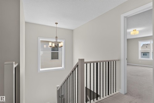 Stairwell featuring a metal baluster railing, an overhead chandelier, and a framed window - 9432 229 Street, Edmonton, AB 