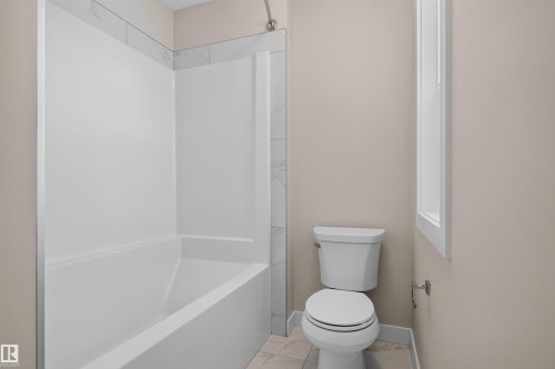 White tub and shower combination with a tile surround, complemented by neutral wall paint and a window with white trim - 9432 229 Street, Edmonton, AB 