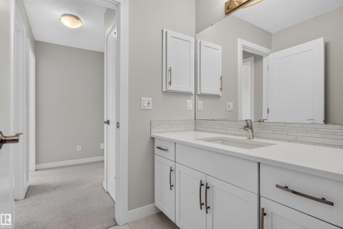 Bathroom vanity featuring white cabinetry, a single basin sink, white countertop, and a white subway tile backsplash - 9432 229 Street, Edmonton, AB 