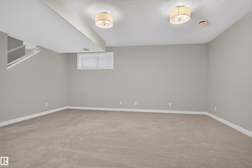 Spacious room featuring neutral carpeting, light gray walls, white baseboards, and two ceiling-mounted drum light fixtures - 9432 229 Street, Edmonton, AB 