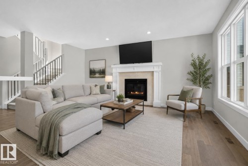 Spacious living area featuring light wood-finish flooring and a central fireplace with a mantel - 9432 229 Street, Edmonton, AB 