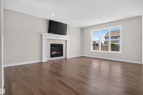 Spacious room featuring a fireplace with a decorative mantel and tiled surround, recessed lighting, wood-finish flooring, and a large window - 9432 229 Street, Edmonton, AB 