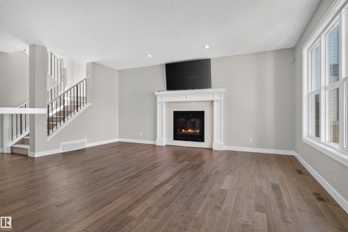 Spacious room featuring wood-finish flooring, a contemporary fireplace with a white mantel, recessed lighting, and large multi-pane windows - 9432 229 Street, Edmonton, AB 