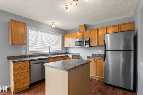 Kitchen featuring wood-finish cabinetry, stainless steel appliances, a central island, laminate countertops, and wood-finish flooring - 7118 19A, Edmonton, AB - Indoor Photo Showing Kitchen With Double Sink