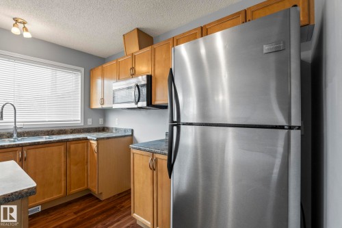 Kitchen featuring wood-finish cabinetry, speckled countertops, stainless steel appliances, and wood-finish flooring - 7118 19A, Edmonton, AB - Indoor Photo Showing Kitchen With Double Sink