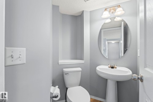 Pedestal sink with chrome faucet, oval mirror, and three-light vanity fixture - 7118 19A, Edmonton, AB - Indoor Photo Showing Bathroom