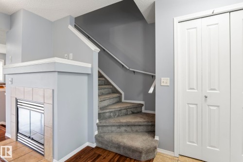 Carpeted staircase with white handrail, gray wall tones, and a built-in fireplace featuring a tiled surround and hearth - 7118 19A, Edmonton, AB - Indoor Photo Showing Other Room
