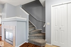 Carpeted staircase with white handrail, gray wall tones, and a built-in fireplace featuring a tiled surround and hearth - 