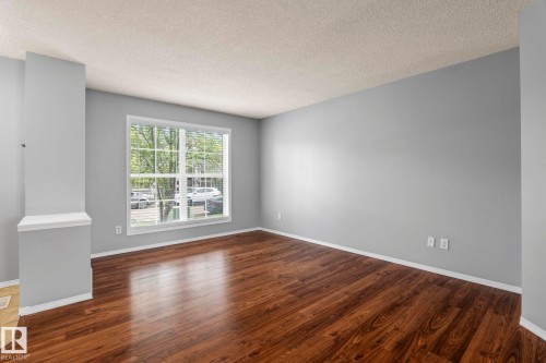 Spacious room featuring wood-finish flooring, light gray wall paint, and a large multi-pane window with horizontal blinds - 7118 19A, Edmonton, AB - Indoor Photo Showing Other Room