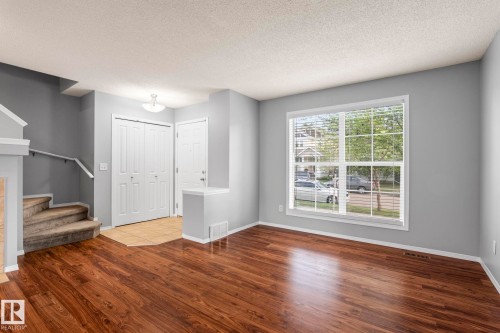 Spacious living area featuring rich wood-finish flooring, a large window with white blinds, and light gray wall paint - 7118 19A, Edmonton, AB - Indoor Photo Showing Other Room