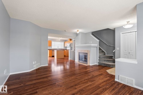 Open concept living area featuring dark wood-finish flooring, a gas fireplace with a light-toned tile surround, and a white mantel - 7118 19A, Edmonton, AB - Indoor Photo Showing Other Room With Fireplace