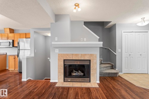 Tiled fireplace with a wood mantle, wood-finish flooring, and built-in closet with bifold doors - 7118 19A, Edmonton, AB - Indoor Photo Showing Living Room With Fireplace