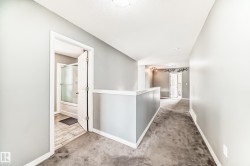 Hallway featuring light gray walls, white baseboards, and gray carpeting - 