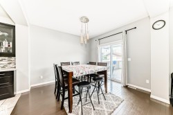 Dining area featuring wood-finish flooring, a modern multi-light pendant fixture, sliding glass door access to an outdoor deck, and a built-in dark wood cabinet with glass-front upper storage and a tiled backsplash - 