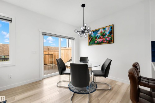 Dining area featuring light wood-finish flooring, a contemporary chandelier, and a sliding glass door opening to an outdoor deck - 3173 Checknita Way, Edmonton, AB 