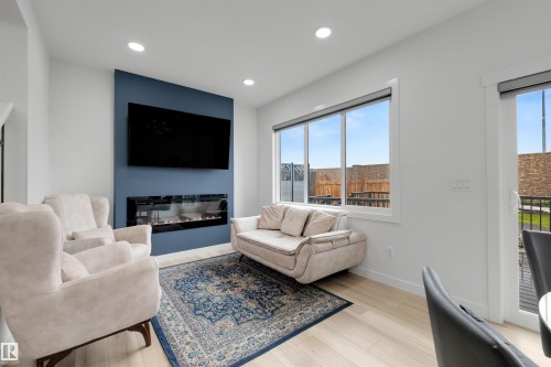 Living area featuring a floor-to-ceiling accent wall with a linear electric fireplace, recessed ceiling lights, and light wood-finish flooring - 3173 Checknita Way, Edmonton, AB 