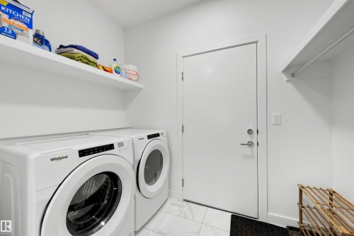 Dedicated laundry area featuring a front-loading washer and dryer, upper wall shelving, and white tile flooring - 3173 Checknita Way, Edmonton, AB 