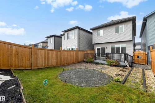 Private backyard featuring a circular paver patio, a raised deck with dark railings, and a wood fence enclosing the perimeter - 3173 Checknita Way, Edmonton, AB 