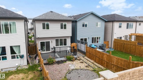 Rear exterior featuring a spacious deck with dark railing, a ground-level patio area, and a fenced yard with grass and gravel landscaping - 3173 Checknita Way, Edmonton, AB 