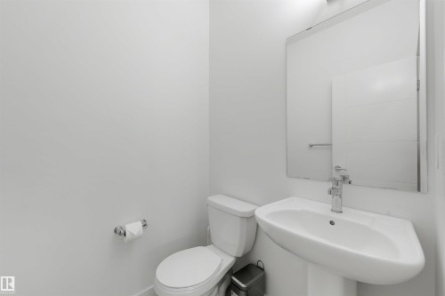 Pedestal sink with chrome faucet, a wall-mounted mirror, and a white toilet - 3173 Checknita Way, Edmonton, AB 
