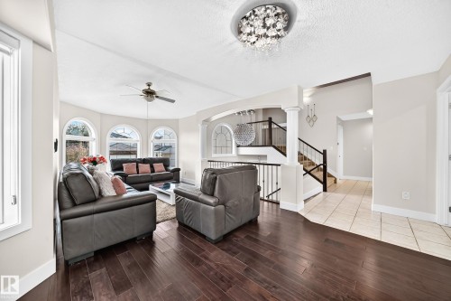Spacious living area featuring dark wood-finish flooring, a contemporary chandelier, and a ceiling fan - 16124 76 Street, Edmonton, AB 