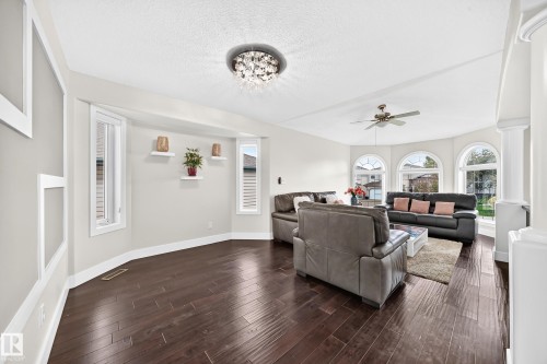 Spacious living area featuring rich wood-finish flooring, a contemporary crystal chandelier, and a ceiling fan - 16124 76 Street, Edmonton, AB 