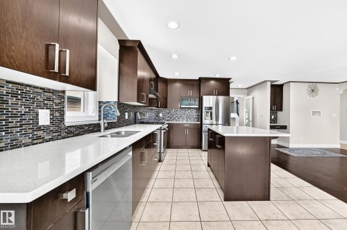 Contemporary kitchen featuring wood-finish cabinetry, stainless steel appliances, a center island with a stone countertop, a mosaic tile backsplash, and recessed lighting - 16124 76 Street, Edmonton, AB 
