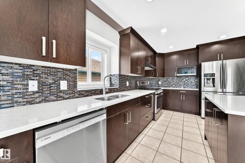 Modern kitchen featuring dark wood-finish cabinetry, stainless steel appliances, and light-toned countertops - 16124 76 Street, Edmonton, AB 