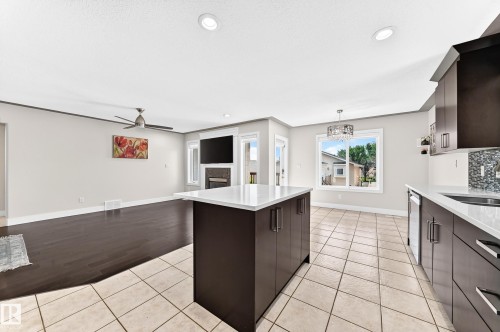 Open-concept living space featuring a central kitchen island with white countertop, dark wood cabinetry, and stainless steel appliances - 16124 76 Street, Edmonton, AB 