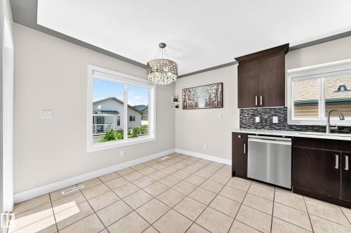 Kitchen area featuring dark wood-finish cabinetry, stainless steel dishwasher, white countertops, and a mosaic tile backsplash - 16124 76 Street, Edmonton, AB 