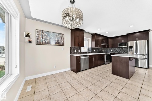 Spacious kitchen featuring extensive dark wood cabinetry, stainless steel appliances, a center island with a light-toned countertop, and tiled flooring - 16124 76 Street, Edmonton, AB 
