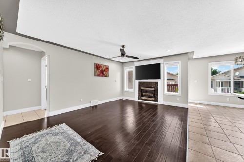 Spacious living area featuring wood-finish flooring, a ceiling fan, and a built-in fireplace with a stone surround - 16124 76 Street, Edmonton, AB 