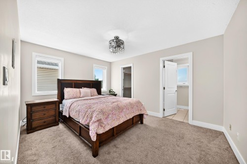 Carpeted room featuring two windows with horizontal blinds, a ceiling-mounted chandelier, and light-toned walls - 16124 76 Street, Edmonton, AB 