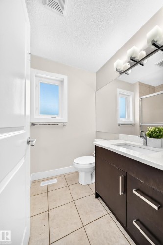 Bathroom featuring a dark wood-finish vanity with a white countertop and integrated sink, a large wall-mounted mirror, square tile flooring, and a window - 16124 76 Street, Edmonton, AB 
