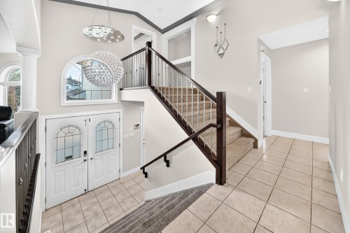 Foyer featuring a dual entry door with decorative glass inserts, an arched transom window, and a multi-tiered crystal chandelier - 16124 76 Street, Edmonton, AB 