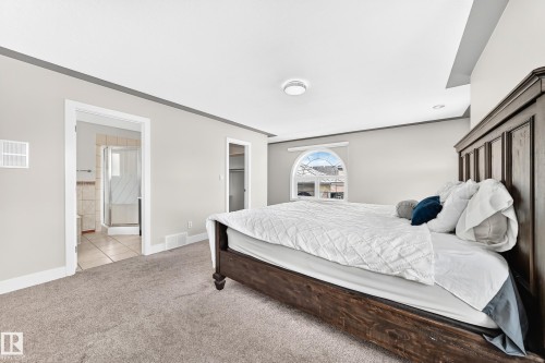 Spacious bedroom featuring light neutral wall tones, arch-top window, recessed lighting, and soft carpet flooring - 16124 76 Street, Edmonton, AB 