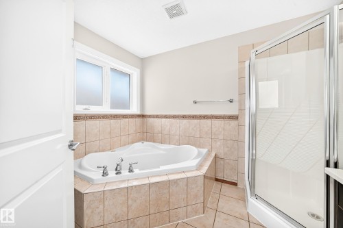 Bathroom featuring a corner soaking tub with deck-mounted fixtures, a glass-enclosed shower, and tiled surround - 16124 76 Street, Edmonton, AB 