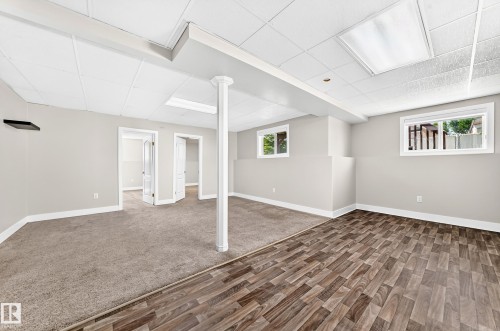 Finished room featuring dual flooring surfaces, light gray walls, white trim, multiple windows, and a grid panel ceiling - 16124 76 Street, Edmonton, AB 