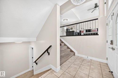 Foyer entry featuring ceramic tile flooring, a white paneled front door with decorative glass inserts, and a black wrought iron staircase railing - 16124 76 Street, Edmonton, AB 