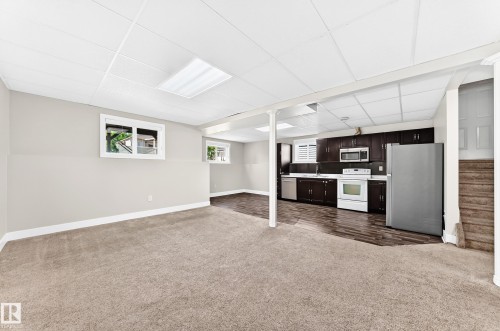 Lower level living area featuring a full kitchen with dark wood-finish cabinetry, stainless steel refrigerator, white range, and built-in microwave - 16124 76 Street, Edmonton, AB 