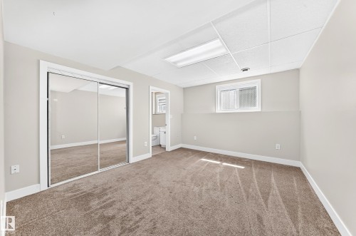 Carpeted room featuring mirrored sliding closet doors, neutral wall paint, white trim, and a drop ceiling with integrated lighting - 16124 76 Street, Edmonton, AB 